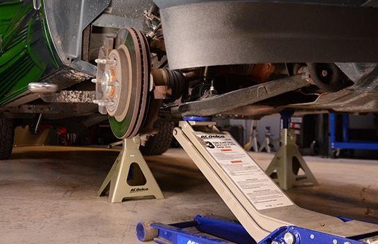 ACDelco Floor Jack positioned under the control arm to support the new strut